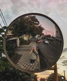 a woman taking a selfie in a mirror on the side of a road at sunset