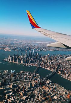 the wing of an airplane flying over a large city and river with tall buildings on both sides