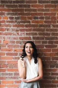 a woman standing in front of a brick wall with her arms crossed and smiling at the camera