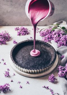 a purple cake being poured into a pie pan with flowers around it and on the table