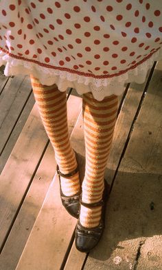 the legs of a woman in striped socks and polka dot tights, standing on a wooden deck