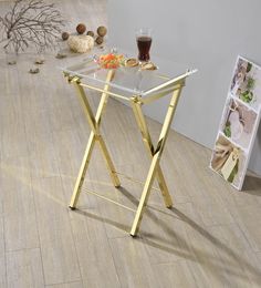 a glass table with gold legs on the floor next to a vase and other items