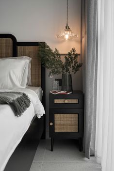 a bed with white sheets and pillows next to a night stand that has a plant on it