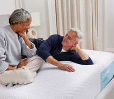 an older man and woman sitting on top of a mattress