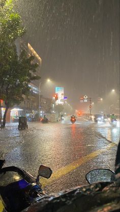 a city street at night in the rain with cars and motorcycles parked on the side