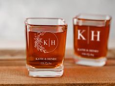 two shot glasses sitting on top of a wooden table next to each other with the initials kh