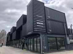 a building made out of shipping containers on the side of a road with people standing outside