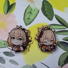 two anime character stickers sitting on top of a flowery surface with leaves and flowers in the background