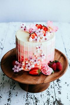 a white cake with strawberries and flowers on a wooden plate next to a knife