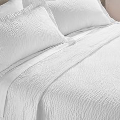 a bed with white sheets and pillows on it