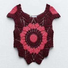 a crocheted top with pink and red circles on the front, sitting on a white surface