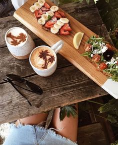 two cups of cappuccino with strawberries and banana slices on the side