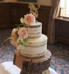 there is a wedding cake on top of a tree stump with pink roses and greenery