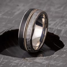 For the groom who loves music, this guitar string ring is a step away from simple wedding bands. A piece of a vinyl record sits in polished titanium with a guitar string, representing the wearer's love of music. Authentic Gibeon meteorite makes this men's wedding band even more of a one-of-a-kind art piece.RING LAYOUT - Vinyl Record Ring with Guitar String and Meteorite-4047 Ring Width: 8.25 mm Ring Sleeve: Titanium Ring Profile: Round Ring Finish: Polished0.5 mm Titanium 3 mm Vinyl LP Record 0. Guitar String Ring, Guitar Wedding, String Ring, Meteorite Wedding Band, Rock N Roll Wedding, Gibeon Meteorite, Meteorite Jewelry, Groom Ring, Simple Wedding Bands