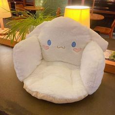 a white stuffed animal chair sitting on top of a table next to a lamp and potted plant