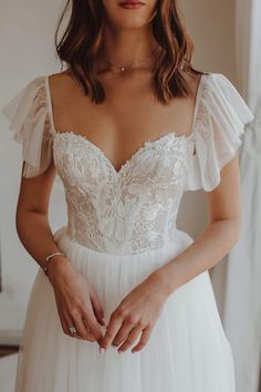 a woman wearing a white wedding dress with ruffle sleeves