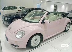 a pink convertible car is on display in a showroom with other cars behind it