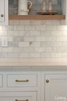 a kitchen with white cabinets and marble counter tops, gold pulls on the cupboards