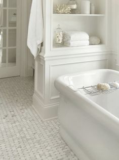 a white bath tub sitting under a window next to a shelf with towels on it