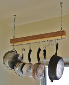 pots and pans are hanging from a rack in front of a window with hooks