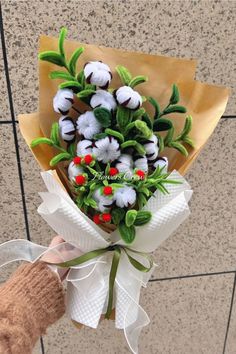 a hand holding a bouquet of flowers with green leaves and red berries on it's stems