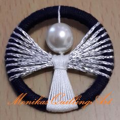 a white pearl on top of a black and white braided ribbon with an angel brooch