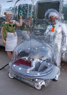 two people dressed as astronauts standing in front of a silver vehicle