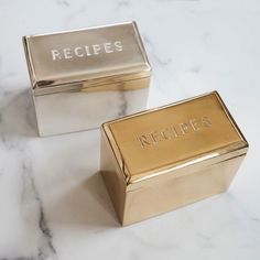 two gold and silver boxes sitting on top of a marble counter