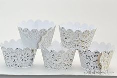 four white lace cupcake cups are lined up on a table with paper doily