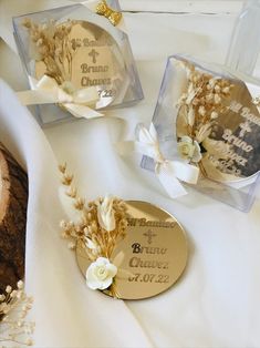 three wedding favors in clear boxes on a white tablecloth with flowers and ribbons around them