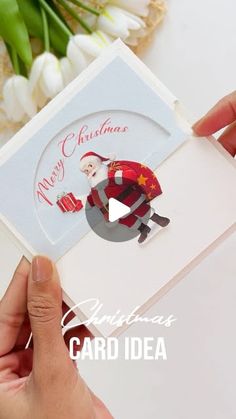 someone holding up a christmas card with a santa clause on it and flowers in the background