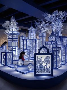 an exhibit with blue and white paper cutouts on the walls, trees, and buildings