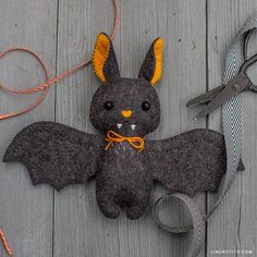 a stuffed animal bat sitting on top of a wooden floor next to scissors and thread