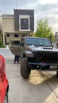 a gray jeep parked in front of a house with two people walking around the driveway