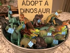 there is a bowl full of dinosaur figurines and a sign that says adopt a dinosaur