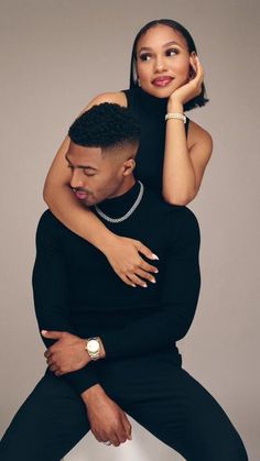 a man holding a woman on his back while she is wearing a black dress and pearls necklace