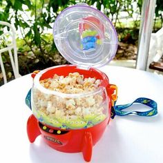 a red bowl filled with popcorn sitting on top of a table next to a plastic toy