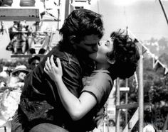 a woman kissing a man on the cheek in front of an amusement park carousel ride