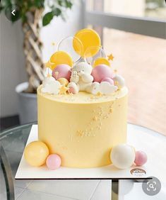 a yellow cake with balloons and stars on top sits on a table in front of a window