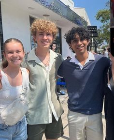 three young people standing next to each other in front of a building and holding up their cell phones