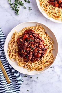 two plates of spaghetti with meat and vegetables on them, next to a blue striped napkin