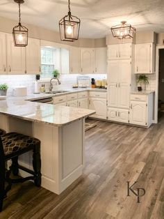 a large kitchen with white cabinets and wooden flooring, lights hanging from the ceiling