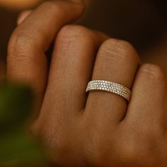 a woman's hand with a diamond ring on her left hand and a green plant in the background