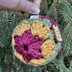 a crocheted ornament hanging from a tree with a hand holding it