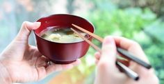 a person holding a bowl of soup with chopsticks