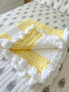 a yellow and white crocheted blanket laying on top of a bed next to pillows