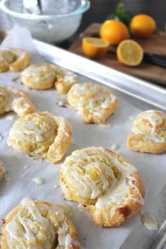 lemon meringue cookies with icing on a baking sheet next to oranges