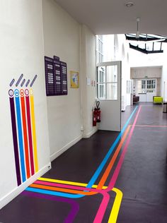 a hallway with colorful lines painted on the floor and white walls, leading to an office building