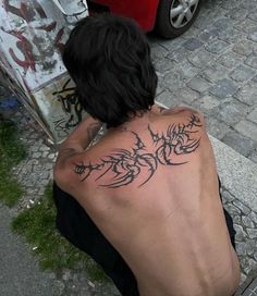 a man sitting on the ground with his back turned to the camera and tattoos on his chest