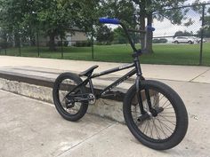 a black bike parked on the side of a road next to a cement wall and fence